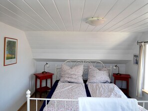 Ein Schlafzimmer mit einem weißen Bett, zwei Nachttischen, einer Deckenleuchte und einem Fenster mit Vorhängen.