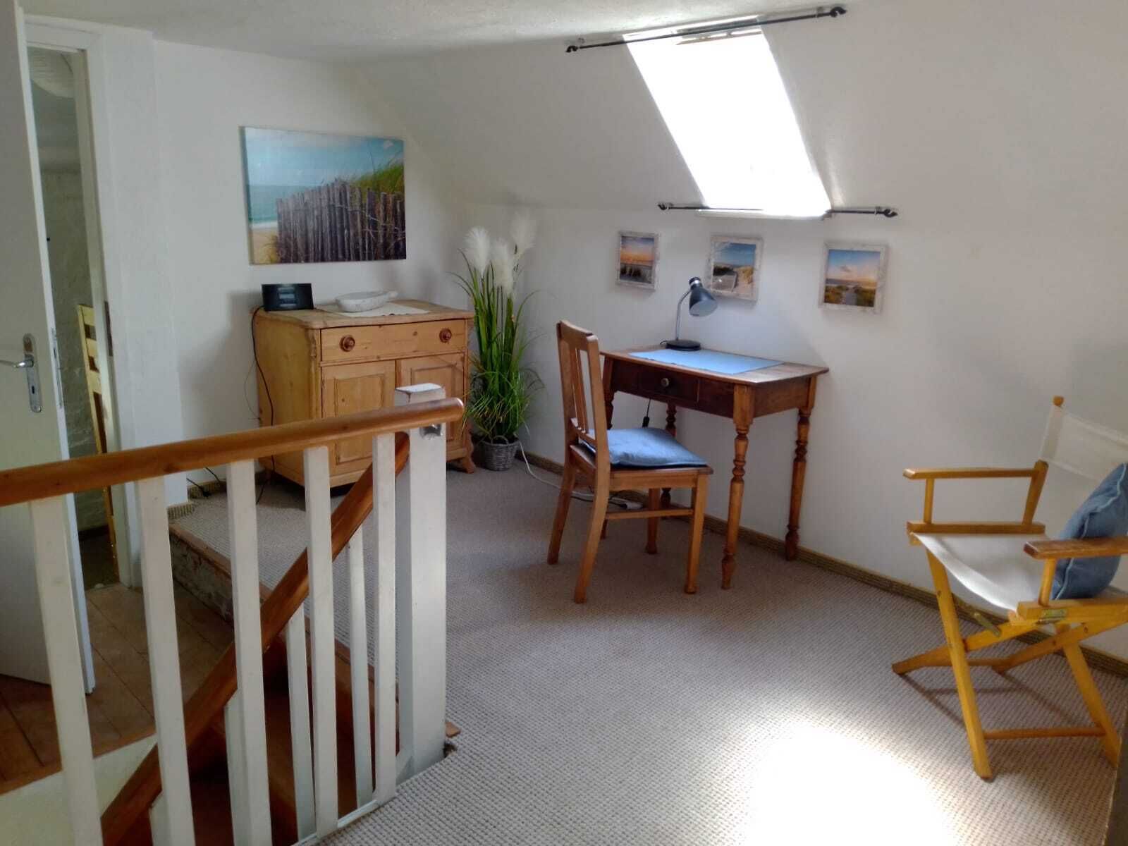 A room with a wooden desk, a chair, a small table, and a potted plant.
