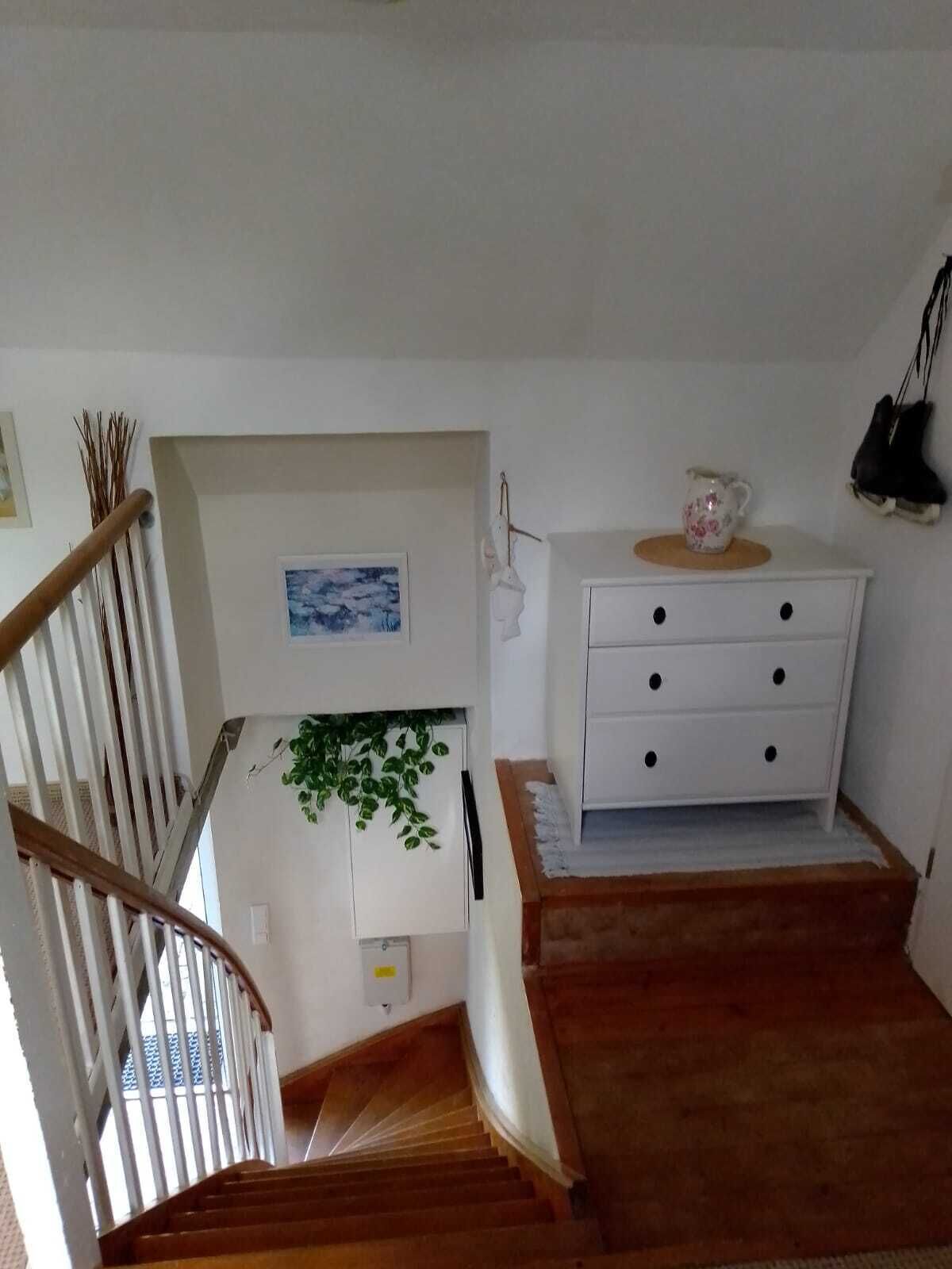 Una escalera conduce a un rellano con un aparador blanco y una mesita con una jarrón floral.