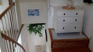 Una escalera conduce a un rellano con un aparador blanco y una mesita con una jarrón floral.