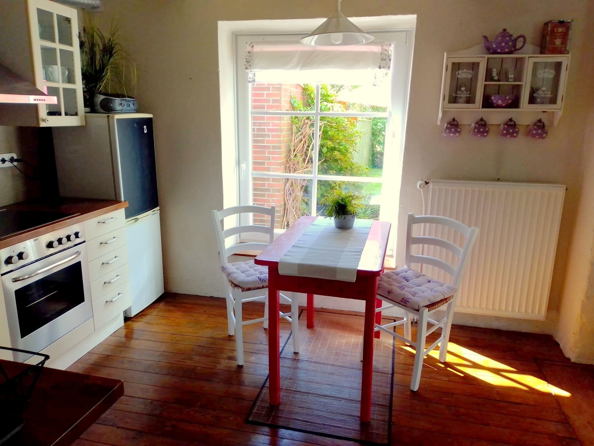 Una cocina con mesa y sillas, un refrigerador, una estufa y un ventanal con vistas al verdor.