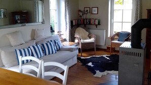Un salon confortable avec un canapé, des fauteuils, une table à manger, une cheminée et une bibliothèque.