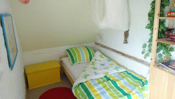 Een knus slaapkamer met een enkel bed, een gele opbergkist, een rode vloerkleed en een houten plank met boeken.