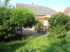 Ein Gartenbereich mit Holztisch und Stühlen, einem gelben Sonnenschirm und einem Backsteinhaus mit Ziegeldach.