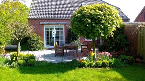 Une maison avec un toit en tuiles, une façade en briques et un jardin agrémenté d’une table et de chaises de patio.