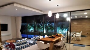 Ein modernes Wohnzimmer mit einem Holzesstisch, weißen Stühlen, einem Sofa und einem an der Wand montierten Fernseher.