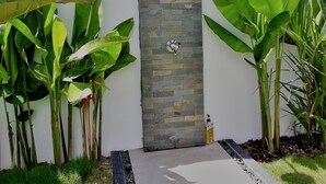 Ein moderner Außenbereich mit Dusche, eine Steinwand und üppige tropische Pflanzen.