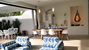 Ein modernes Wohnzimmer mit einer großen Eckcouch, einem Essbereich mit Holztisch und Stühlen sowie einer Küche mit weißen Schränken und einer Pendelleuchte.