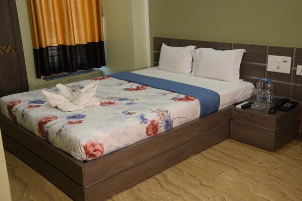 Una habitación de hotel con una cama, una mesita de noche y un ventanal con cortinas.