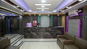 A hotel reception area with a marble reception desk, two receptionists, a fire alarm, and a no smoking sign. - Hotel Nandini (Baharampur)