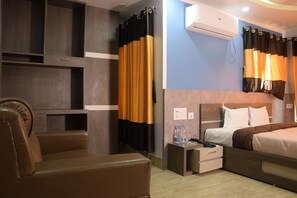 A hotel room with a bed, a chair, a small table, an air conditioning unit, and a curtain. - Hotel Nandini (Baharampur)