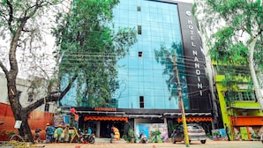 A modern hotel with a glass facade, a restaurant on the ground floor, and a tree in front. - Hotel Nandini (Baharampur)