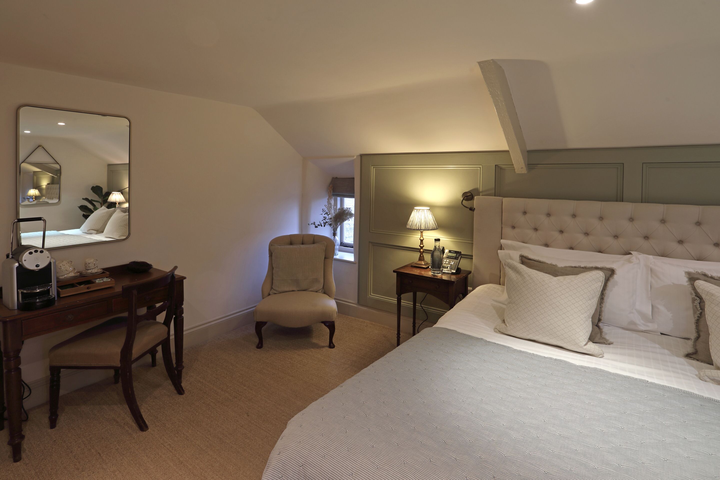 A hotel room with a bed, a desk, a chair, a lamp, and a mirror.