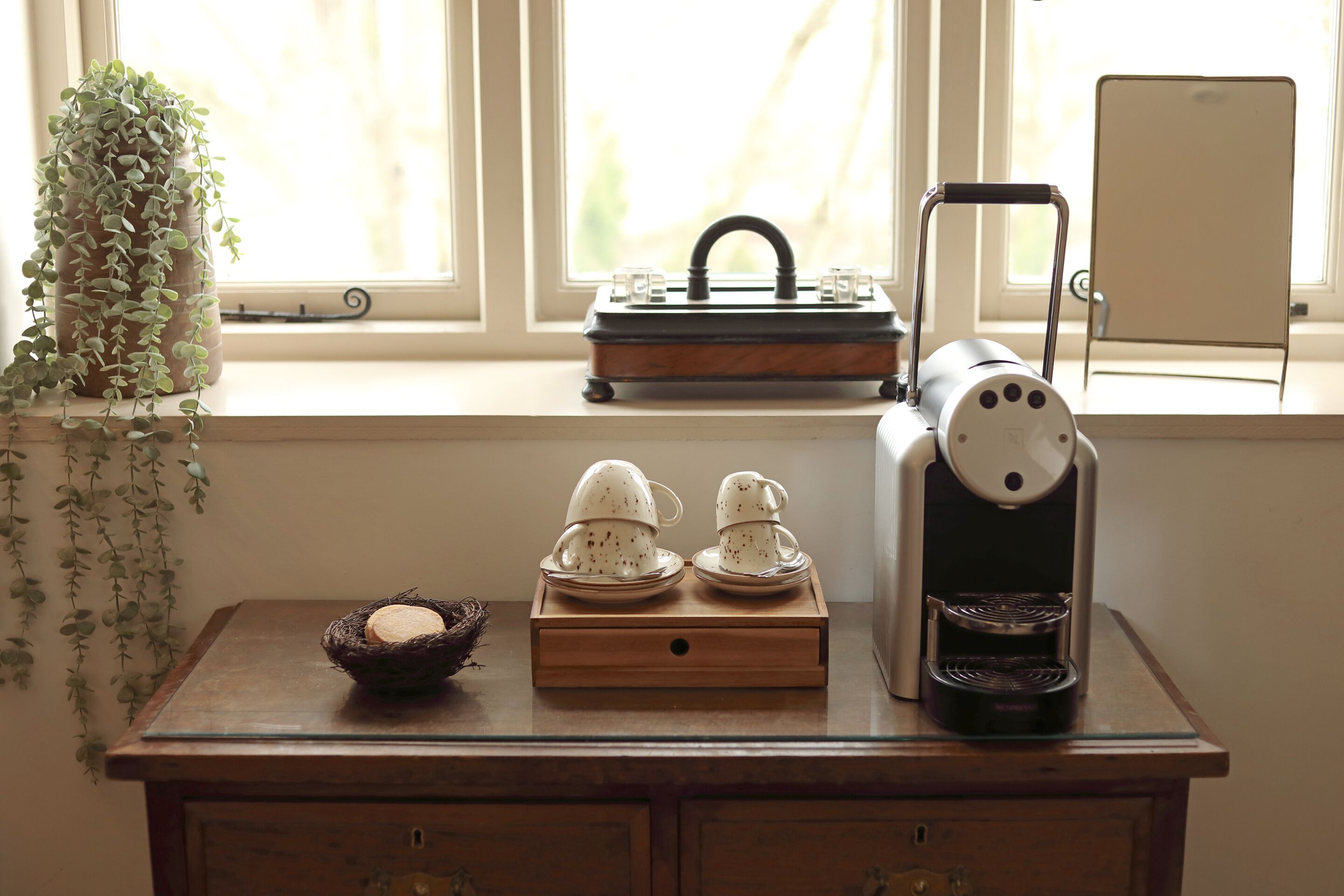 A wooden table with a coffee maker, a tray of teacups, and a small birdcage with a nest.