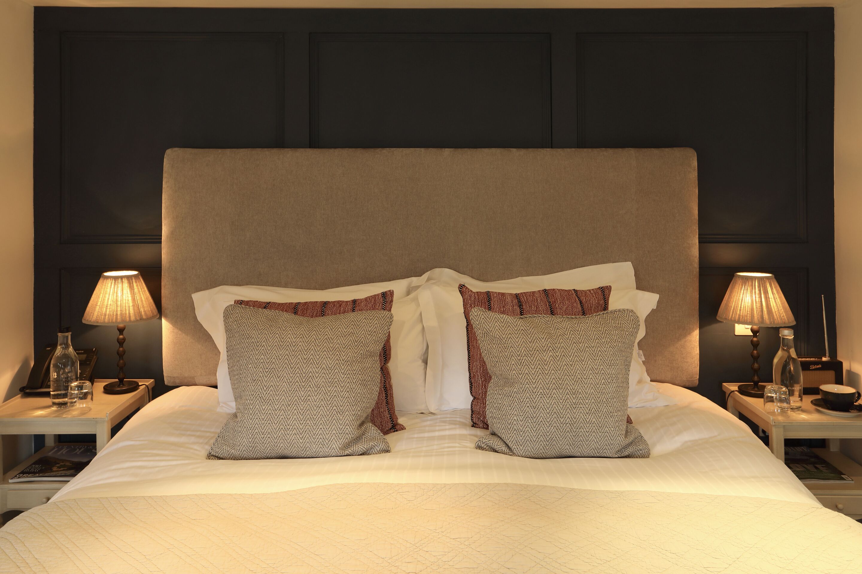 A neatly made bed with a large headboard, two bedside lamps, and patterned pillows.