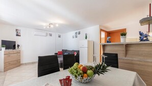 Una cucina moderna con zona pranzo, con una ciotola di frutta sul tavolo, un frigorifero e una TV.