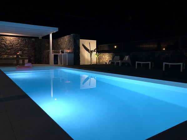 A swimming pool with a stone wall and a covered patio area. - Brand new and modern villa in Lajares (Fuerteventura) with heated pool (Lajares - Fuerteventura)