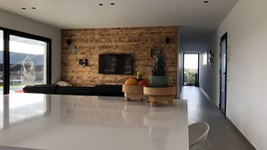 A modern living room with a wooden wall, a large TV, and a central island with fruit bowls. - Brand new and modern villa in Lajares (Fuerteventura) with heated pool (Lajares - Fuerteventura)