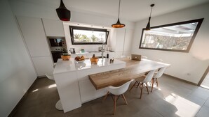 A modern kitchen with a central island, white cabinetry, and a dining area with a wooden table and white chairs. - Brand new and modern villa in Lajares (Fuerteventura) with heated pool (Lajares - Fuerteventura)