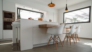 A modern kitchen with a central island, white chairs, and a dining table. - Brand new and modern villa in Lajares (Fuerteventura) with heated pool (Lajares - Fuerteventura)