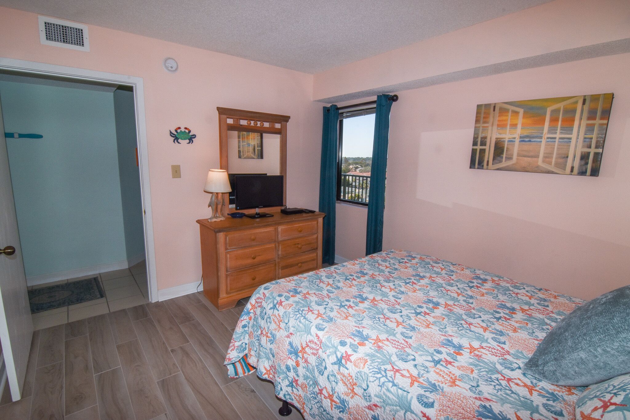 Un dormitorio con cama, cómoda, televisor y un cuadro.