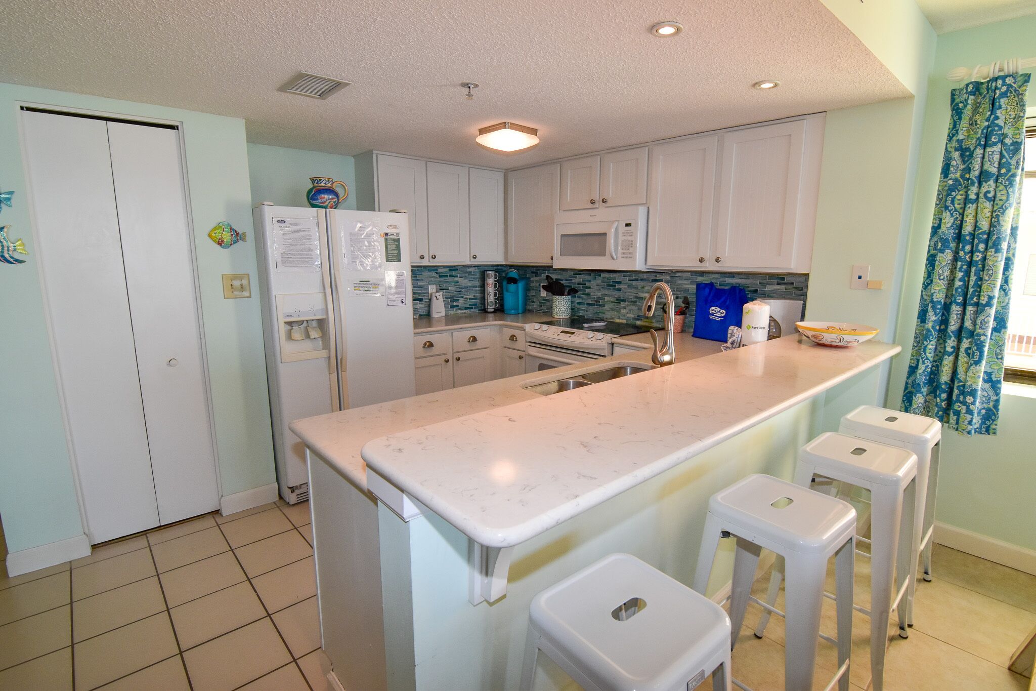 A kitchen with white cabinets, a white refrigerator, a microwave, a sink, and a bar stool.