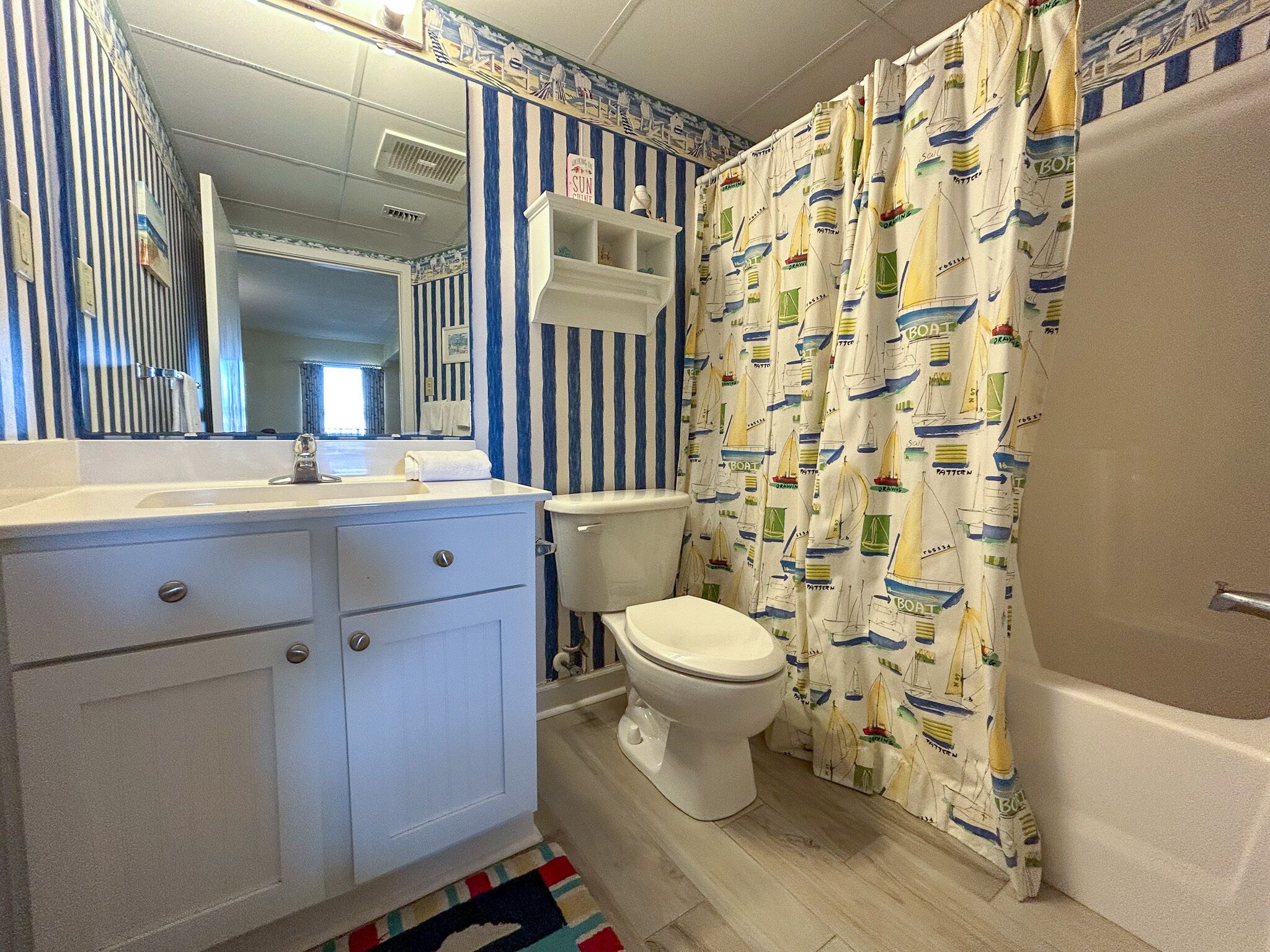 A bathroom with a striped wall, a toilet, a sink, and a shower curtain with a boat pattern.