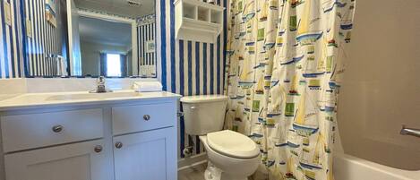 A bathroom with a striped wall, a toilet, a sink, and a shower curtain with a boat pattern.