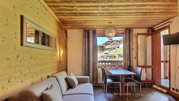 Una camera accogliente con soffitto in legno, un divano, un tavolo da pranzo con sedie e un'ampia finestra vista su un edificio.