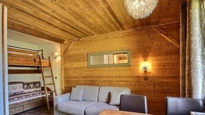 Una stanza accogliente con soffitto in legno, un divano, un tavolo e un letto a castello con una scala.