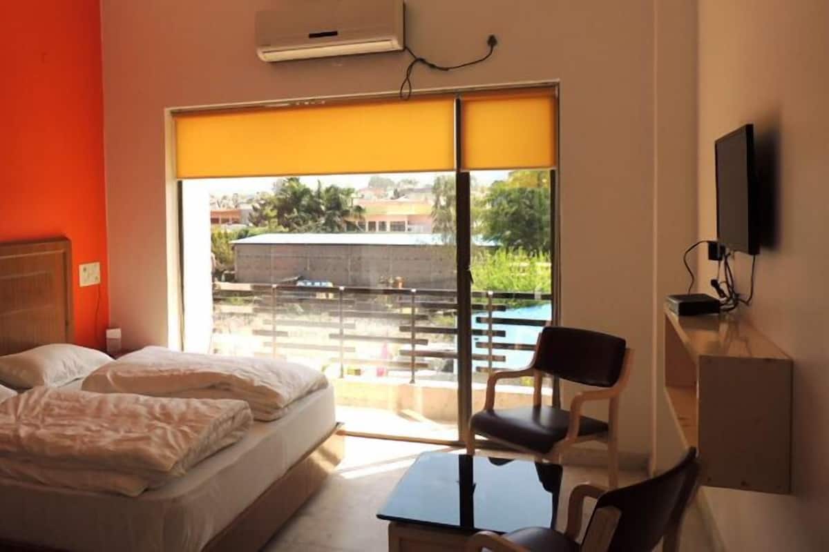 A hotel room with a bed, a desk, a chair, a TV, and a large window with a view of the outside.