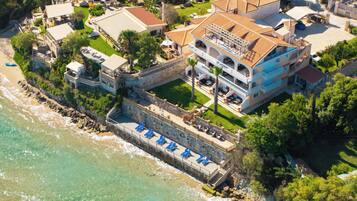 An aerial view of a coastal property with a large building, a swimming pool, and a beach area.