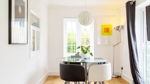 Een eethoek met een glazen tafel, twee stoelen, een potplant en een moderne hanglamp.