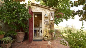 Un edificio rustico in pietra con una porta rossa, piante in vaso e cesti di fiori appesi.