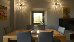 Zona pranzo con tavolo in legno, quattro sedie, una ciotola e due lampade a parete.
