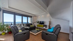 A modern living room with a sofa, two armchairs, a coffee table, and a TV. Large windows offer a view of the sea. - Stunning home in Crikvenica (Crikvenica)