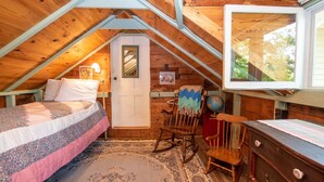 A cozy attic bedroom with a bed, rocking chair, dresser, and a window with a view of trees. - Ironwood: Amazing Keuka Lake Views! (Hammondsport)