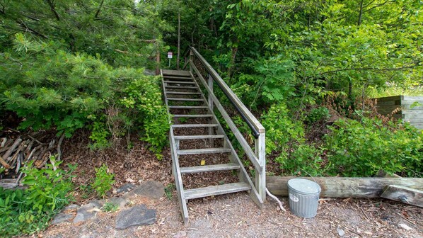 A wooden staircase leading up a forested area with a metal trash can at the bottom.