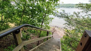 A wooden staircase leading down to a lakeside path, surrounded by trees and vegetation. - Ironwood: Amazing Keuka Lake Views! (Hammondsport)