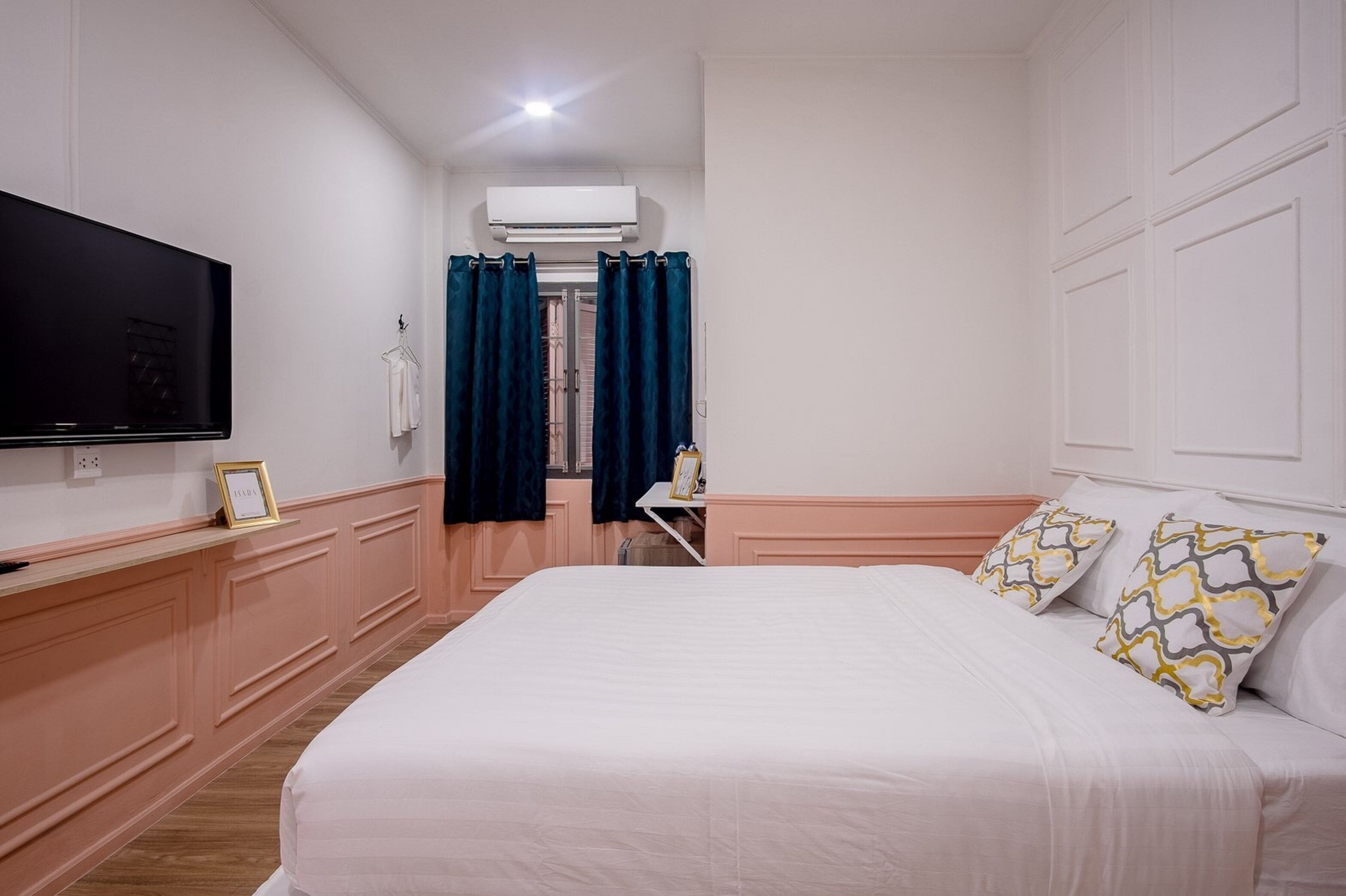 Une chambre à coucher avec un lit, une télévision, un bureau et une fenêtre avec des rideaux.