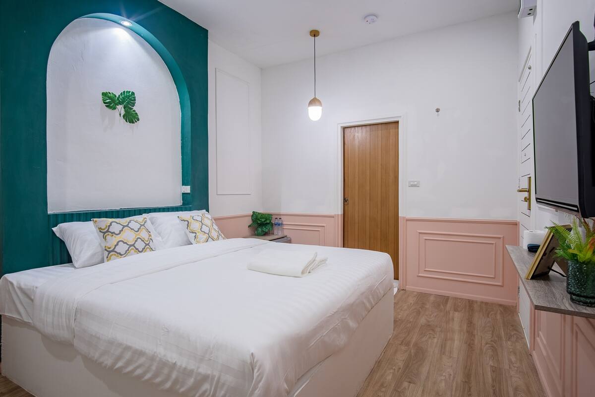 Un llit ben fet amb llençols blancs, una paret d'accent color aguamarina, una porta de fusta i una petita taula de nit amb una planta.