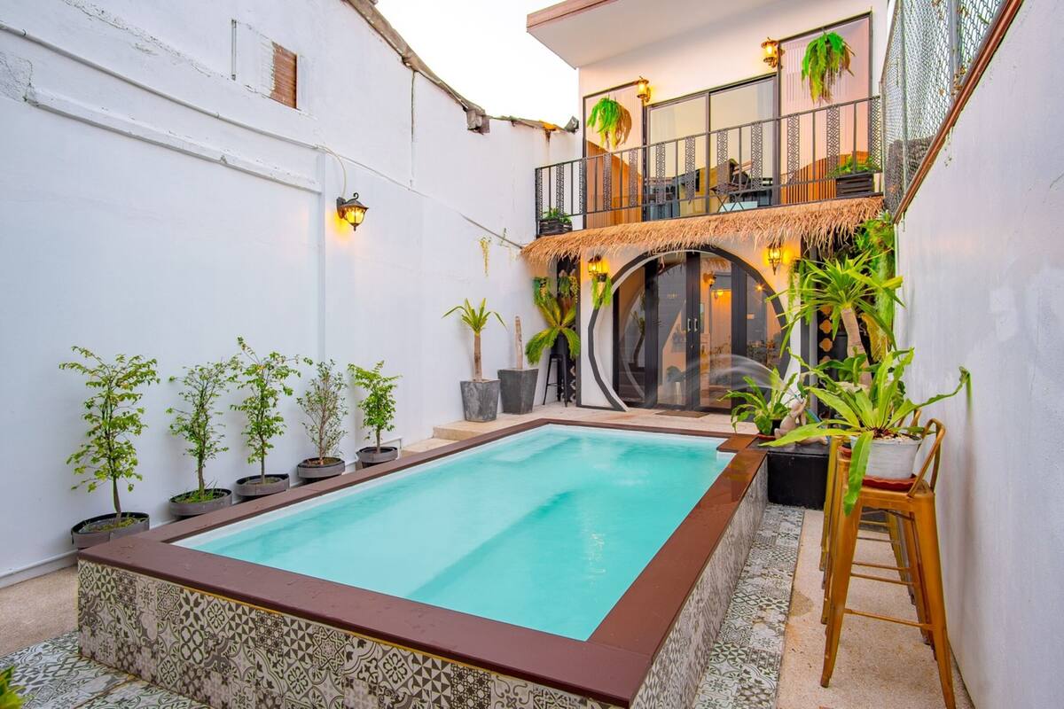 Una piscina amb un videt de rajola, envoltada de plantes en testos i una escala que porta a un nivell superior.