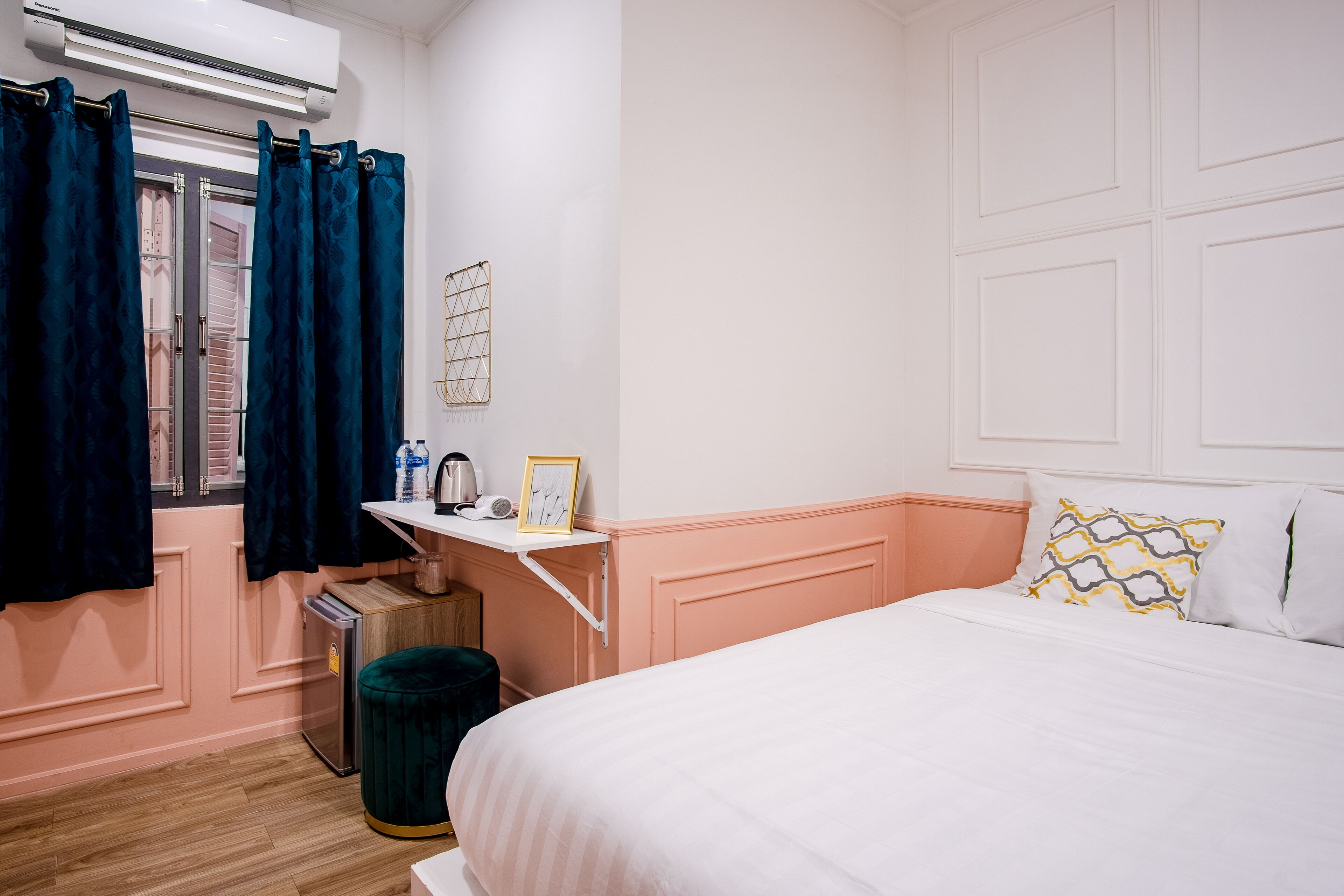 Un dormitorio con cama, mesita de noche, ventana con cortinas, aire acondicionado de pared y un cubo de basura pequeño.