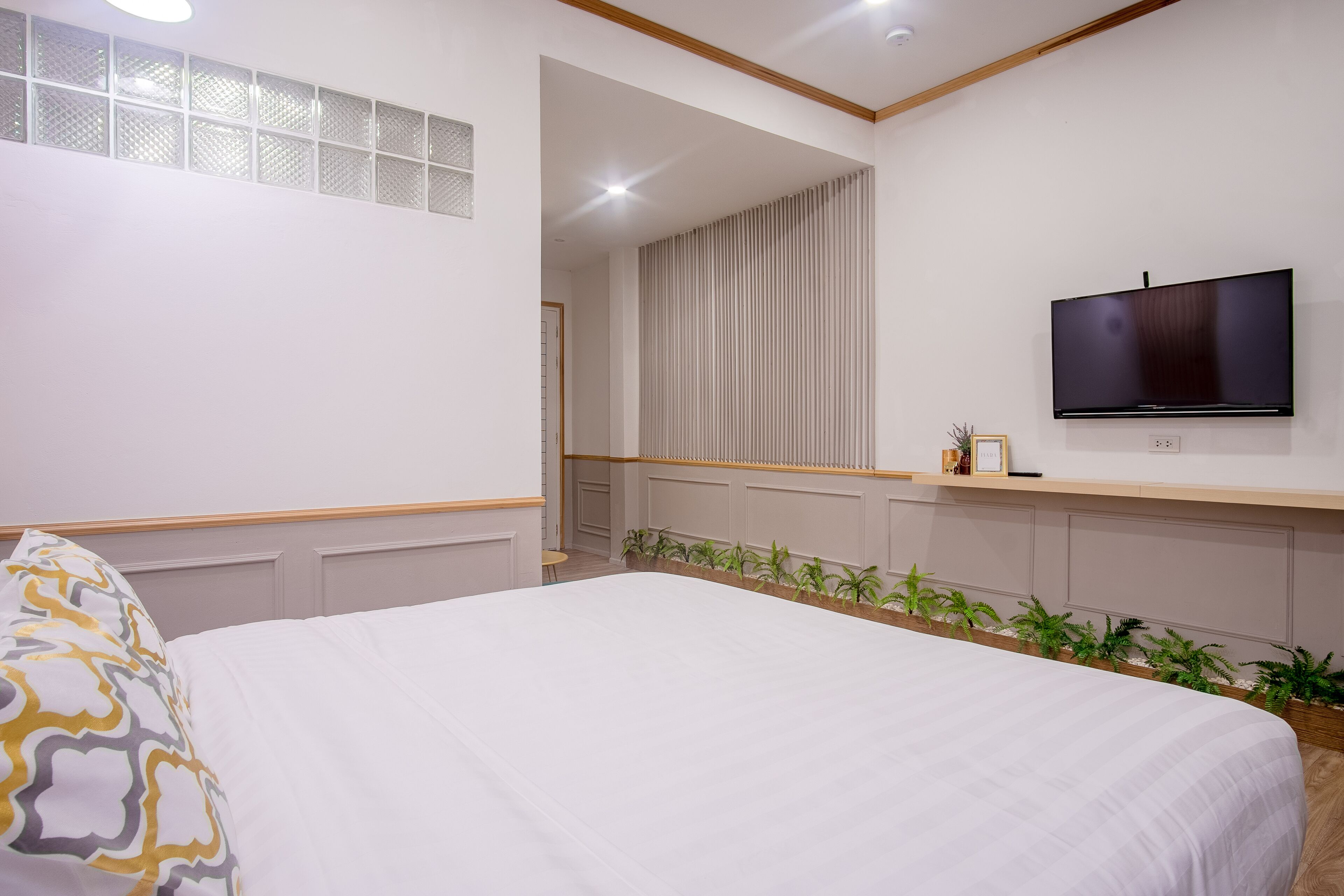 Une chambre d’hôtel avec un grand lit, un téléviseur à écran plat fixé au mur, une petite table avec une plante et une fenêtre avec des stores.