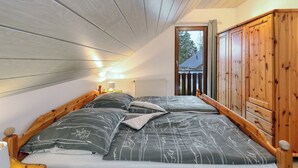 A bedroom with a sloped ceiling, wooden headboard, and a view of the outside through a door. - Cottage near Diane (lake, forest, wellness) (Kirchheim)