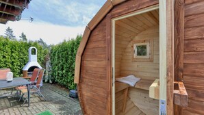 A wooden cabin with a small sleeping area, a dining table, and a wood-fired oven. - Cottage near Diane (lake, forest, wellness) (Kirchheim)