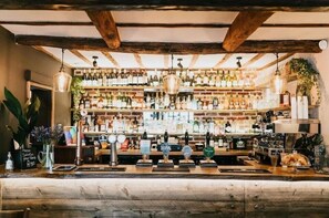 Un bar con vigas de madera, estantes llenos de botellas y una barra con grifos.