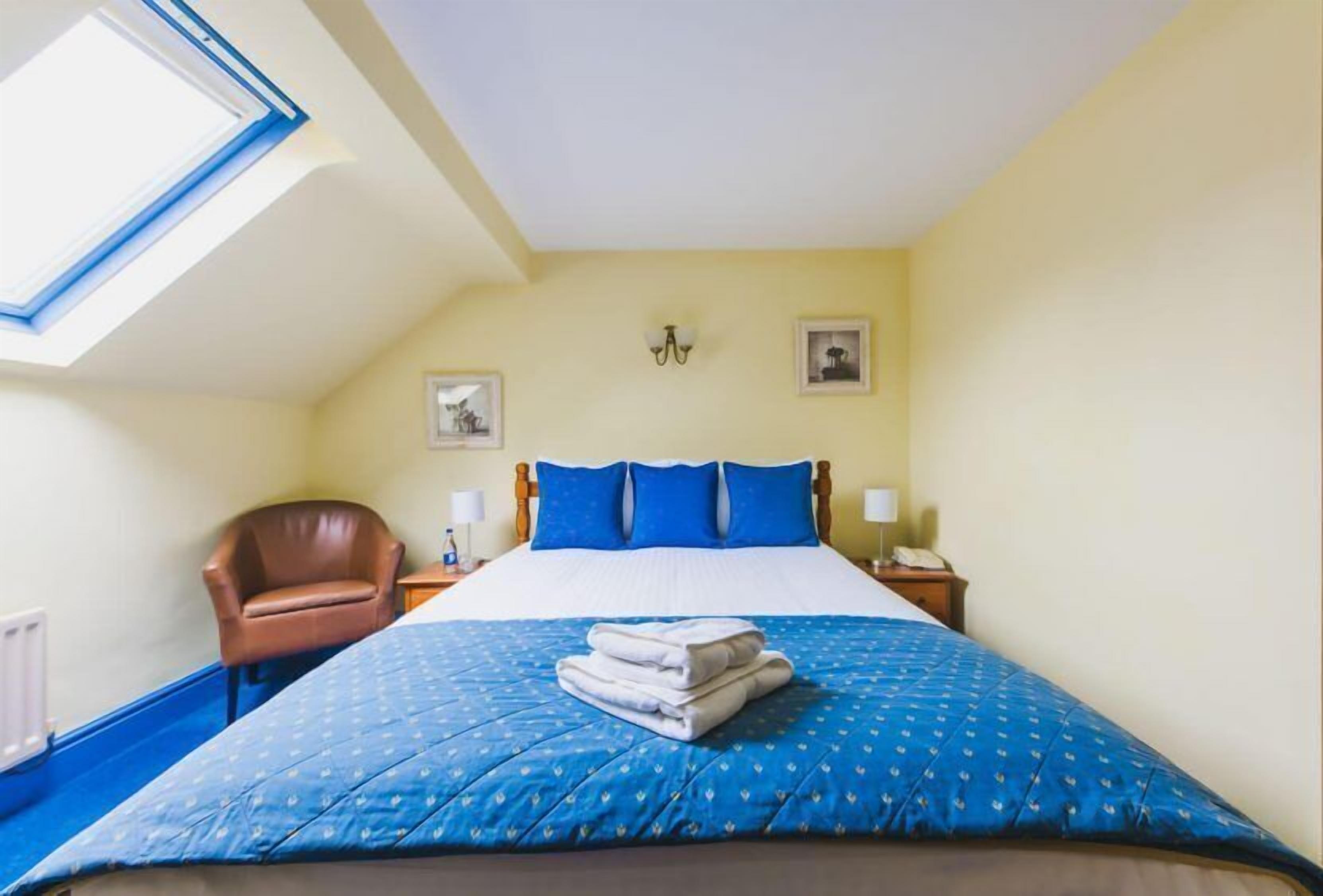 A bedroom with a bed, a chair, a nightstand, and a wall-mounted lamp.