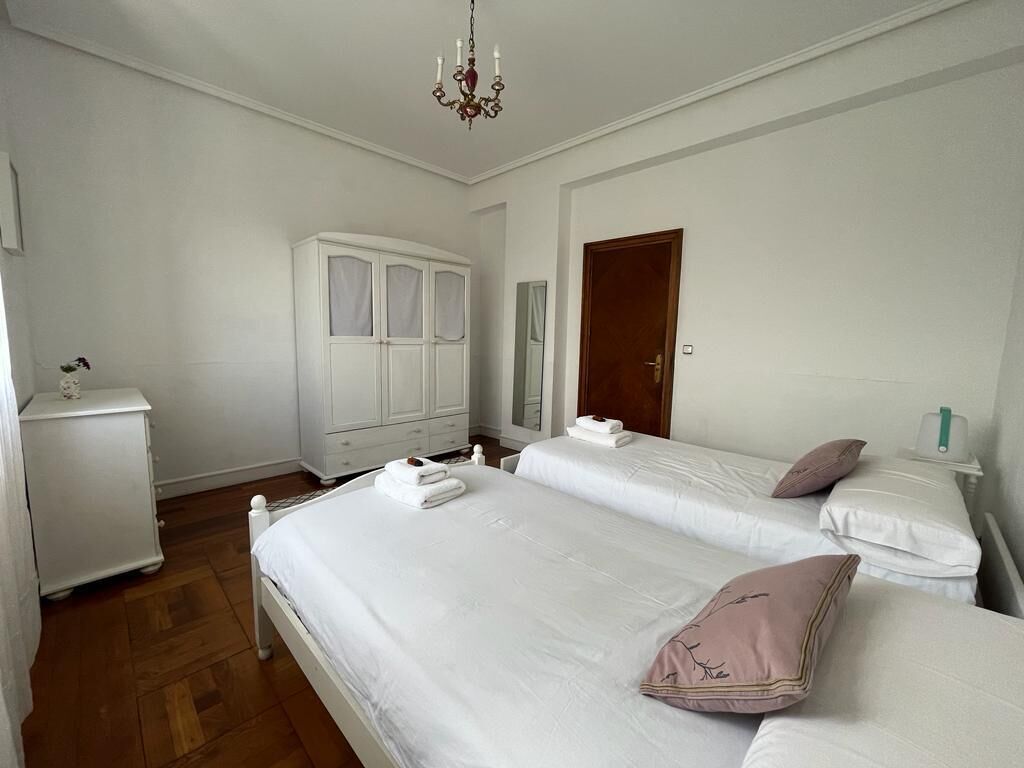 A bedroom with two beds, a wardrobe, a nightstand, and a chandelier.