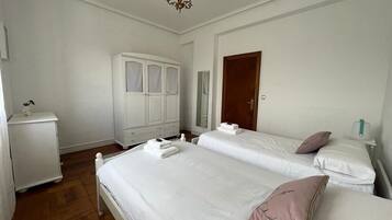 A bedroom with two beds, a wardrobe, a nightstand, and a chandelier.